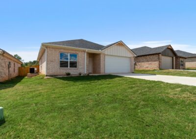 Single-story brick house with a two-car garage, green lawn, and a driveway, under a clear blue sky in a suburban neighborhood.