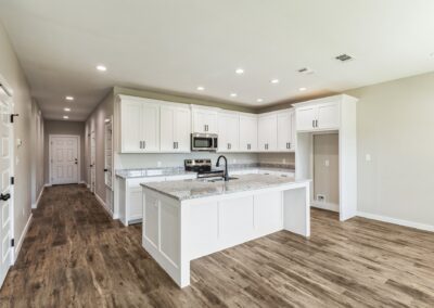 Modern kitchen with white cabinets, granite countertops, an island with a black faucet, stainless steel appliances, and wood-look flooring. Bright and spacious with recessed ceiling lights.